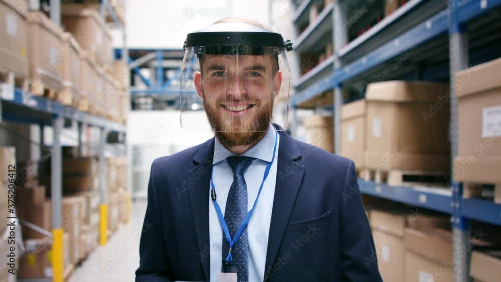 Man manager with protective face shield and tablet walking in warehouse. Man manager with protective face shield and tablet walking in warehouse.