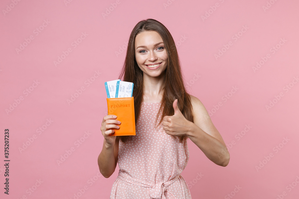 Smiling young brunette traveler tourist woman 20s wearing pink summer dotted dress posing hold passport tickets boarding pass showing thumb up isolated on pastel pink wall background studio portrait. Smiling young brunette traveler tourist woman 20s wearing pink summer dotted dress posing hold passport tickets boarding pass showing thumb up isolated on pastel pink wall background studio portrait.