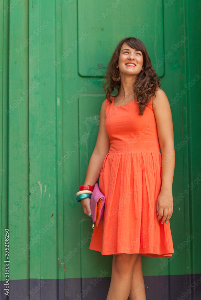 Woman in an orange dress standing against green wall. Woman in an orange dress standing against green wall.