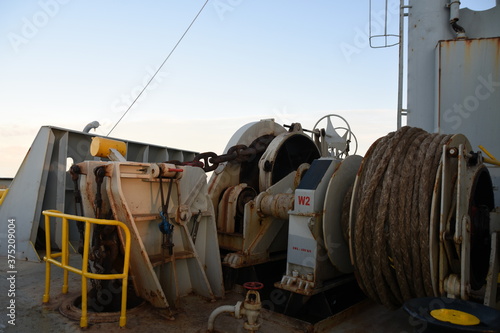 Obraz na plátně Forward port side mooring winch and anchor windlass with heaved up white aged manila rope on working drum of cargo container vessel during passing  Atlantic ocean in time of sunset