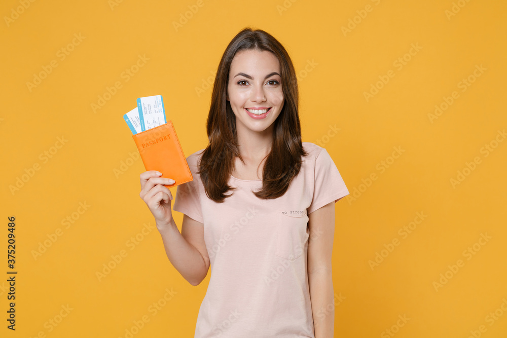 Smiling young brunette traveler tourist woman in pastel pink casual t-shirt posing looking camera hold passport tickets boarding pass isolated on bright yellow color wall background studio portrait. Smiling young brunette traveler tourist woman in pastel pink casual t-shirt posing looking camera hold passport tickets boarding pass isolated on bright yellow color wall background studio portrait.