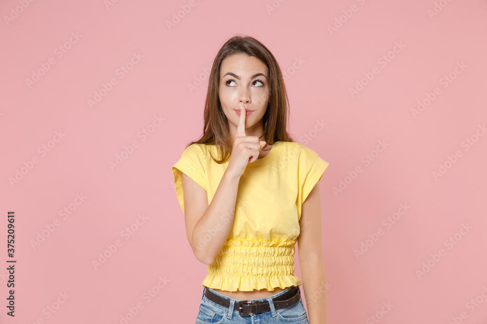 Secret young brunette woman 20s wearing yellow casual t-shirt posing standing saying hush be quiet with finger on lips shhh gesture looking up isolated on pastel pink color background studio portrait. Secret young brunette woman 20s wearing yellow casual t-shirt posing standing saying hush be quiet with finger on lips shhh gesture looking up isolated on pastel pink color background studio portrait.