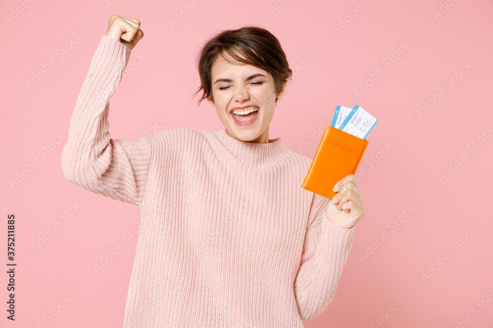 Happy young woman in casual sweater isolated on pastel pink background. Passenger traveling abroad to travel on weekends getaway. Air flight journey concept. Hold passport ticket doing winner gesture. Happy young woman in casual sweater isolated on pastel pink background. Passenger traveling abroad to travel on weekends getaway. Air flight journey concept. Hold passport ticket doing winner gesture.