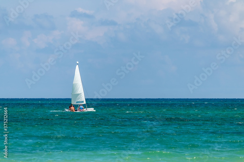 Nautical background of a white sailboat in bright sunlight, on blue ocean water, with space for text