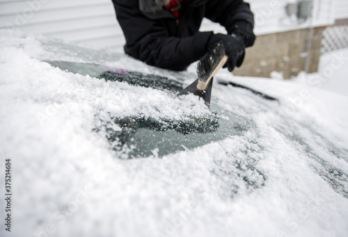 Man scrapes ice and snow off the windshield of his car in winter