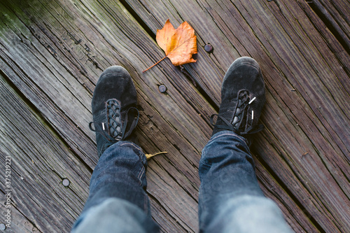 Looking down on a leaf between two feet wearing sneakers. photo