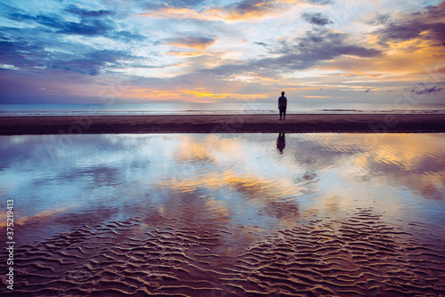 The atmosphere of the sun of the beach where the water and the sky reflect, making the person standing in the distance as if in the middle of the sky.