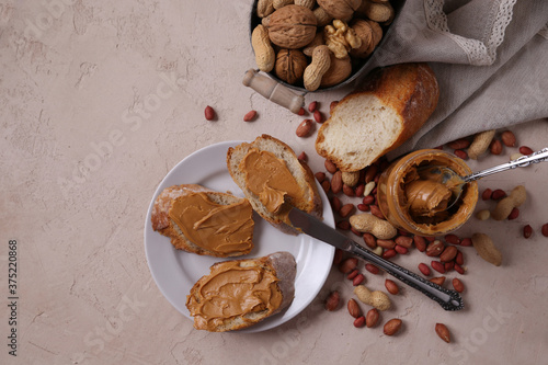 Peanut butter in a jar with bread on a white plate, peanut butter sandwich, nuts scattered on the table. walnuts. Still life, home cooking concept