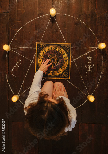 Woman sitting inside a pentagram using a Ouija board. photo
