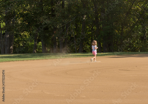 Φωτογραφία Small toddler girl playing in the sand and dirt of an empty baseball field in th