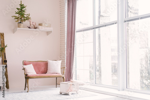 A pink vintage sofa with pillows stands near the window in the living room or children's room, decorated for Christmas or New Year, in the house. Minimalistic interior design