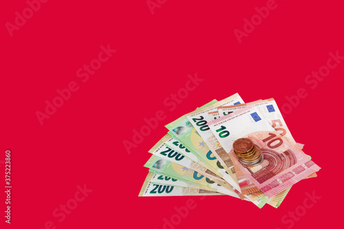 Bundle of cash money,10,50,100,200 Euro paper banknotes and column of stacked Euro coins of various denominations on top on bright red backdrop.Concept of real money,call to action.Large copy space.