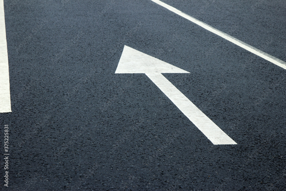 Arrow sign on the road. White arrow on the asphalt. White forward arrow on a blurry street background