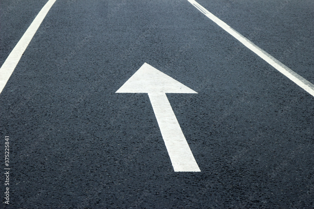 Arrow sign on the road. White arrow on the asphalt. White forward arrow on a blurry street background