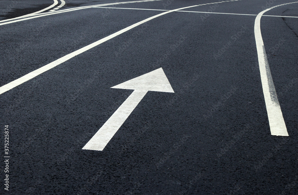 Arrow sign on the road. White arrow on the asphalt. White forward arrow on a blurry street background