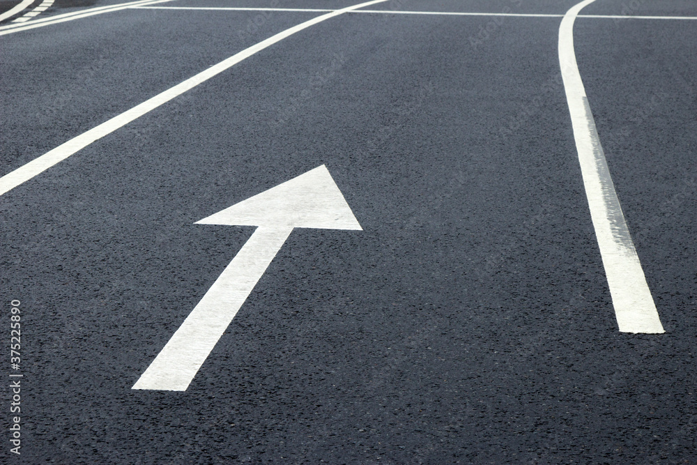 Arrow sign on the road. White arrow on the asphalt. White forward arrow on a blurry street background