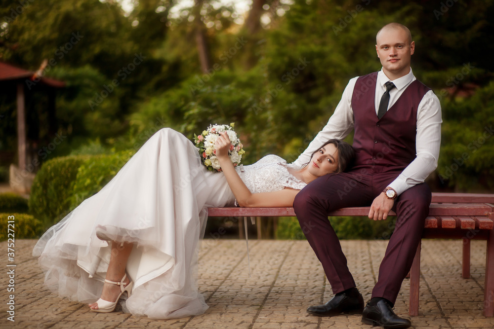Portrait of a happy wedding couple on their wedding day,beautifully dressed newlyweds tenderly hug while walking in a park, handsome groom gently hugs his bride. Newlyweds sit on a bench