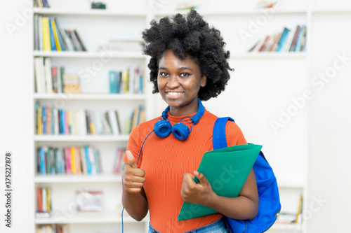 Afro american female college student with backpack and paperwork showing thumb up photo