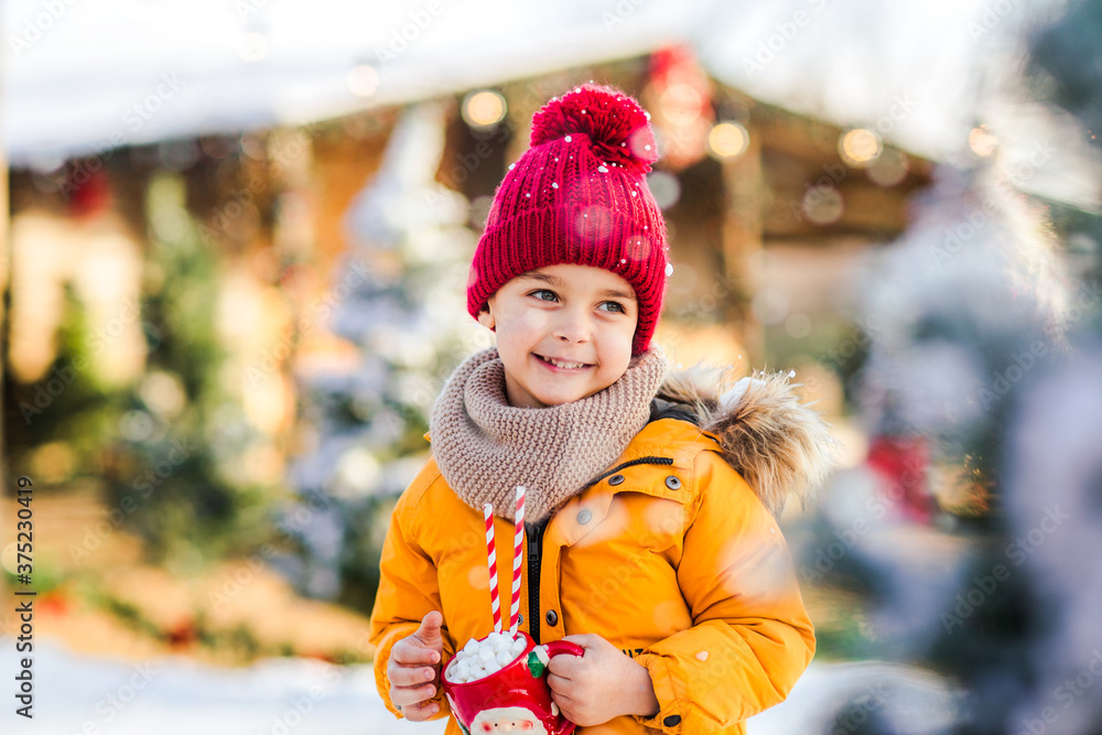 Young boy holding Santa's cup of cacao with marshmallows standing on a fake ice rink. Young boy holding Santa's cup of cacao with marshmallows standing on a fake ice rink.