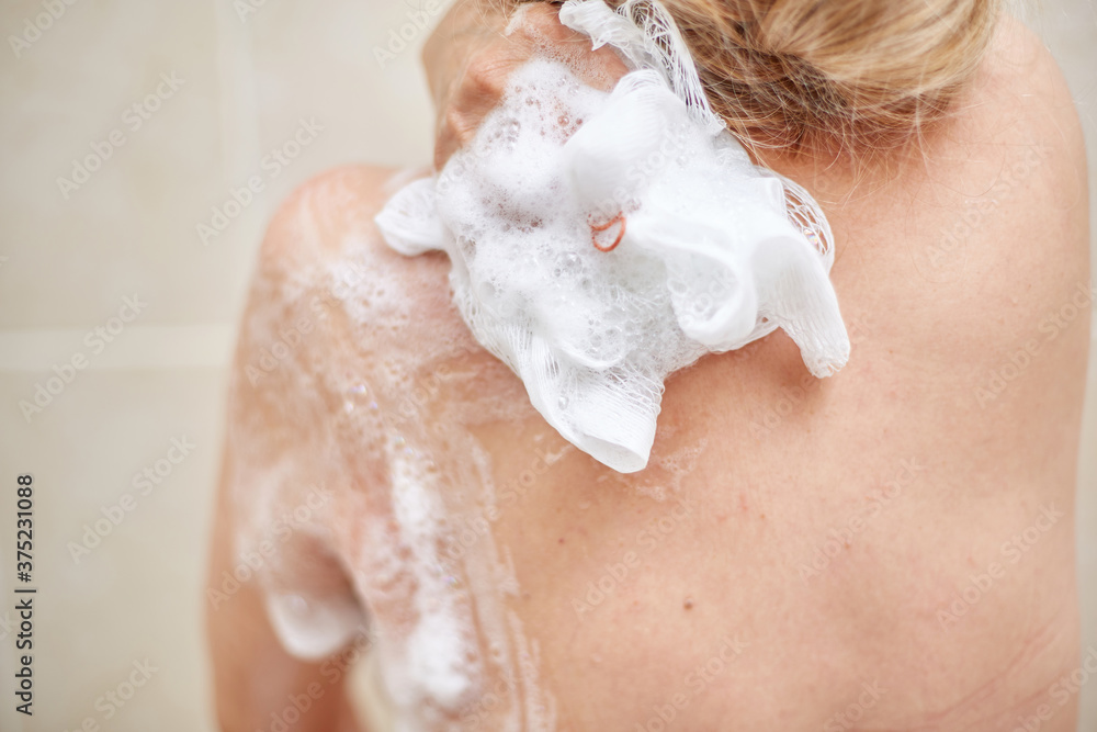 Fototapeta premium an elderly 60-year-old woman washes in the shower, Soaps her shoulders, back and body with a washcloth in the home bathroom