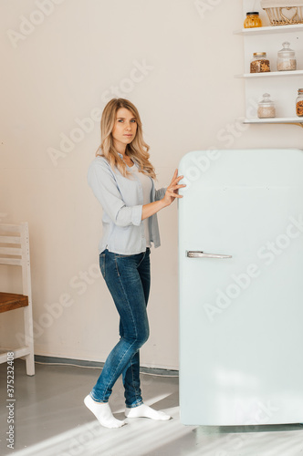 girl opens the door of the refrigerator. Beautiful kitchen.