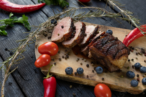 Goose breast Christmas roast with blueberries, tomatoes, red peppers and rosemary served on a wooden board photo