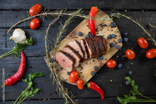 Goose breast Christmas roast with blueberries, tomatoes, red peppers and rosemary served on a wooden board photo