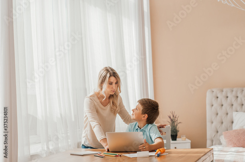 Warm-toned portrait of young mother talking to son while doing homework together sitting at table in cozy kitchen interior, copy space