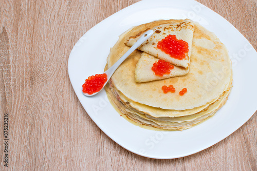 Pancakes with red caviar. Pancakes with caviar on a white plate. Pancakes with red caviar on a plate and a wooden board.