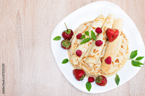 Pancakes with strawberries and raspberries. Pancakes with raspberries and strawberries on a plate. Pancakes with raspberries and strawberries on a plate and a wooden board.