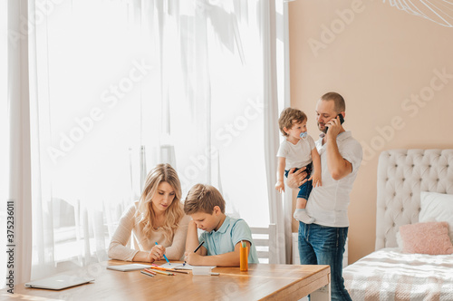 Parents reading books while siblings writing in exercise books on floor in apartment