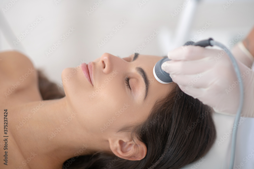 Fototapeta premium Young woman lying down with eyes closed during professional beauty procedures