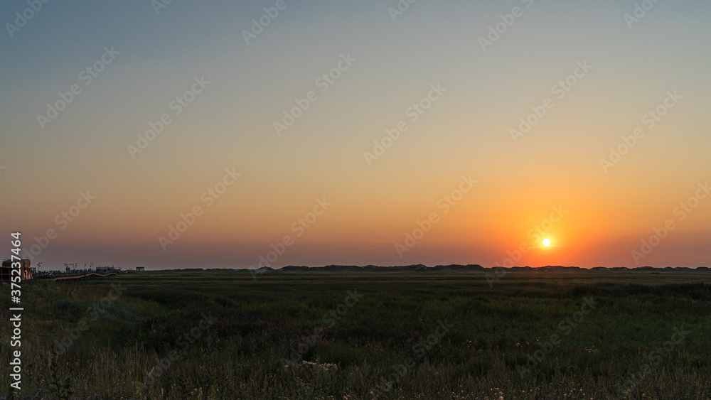 Wide view of the sunset over the grassland between the dike and the beach on the North Sea coast.