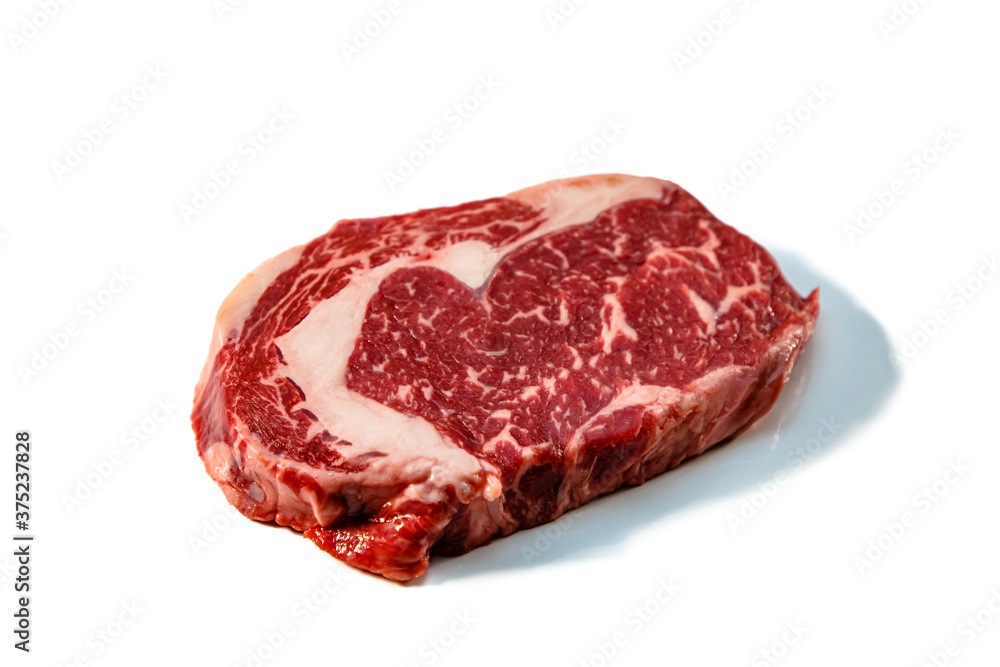 Obraz premium Ribeye. A raw marbled beef steak sits on a white background with a shadow.