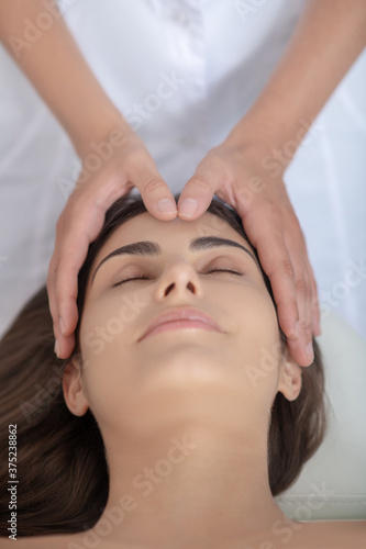 Professional massage therapist putting hands on customers head