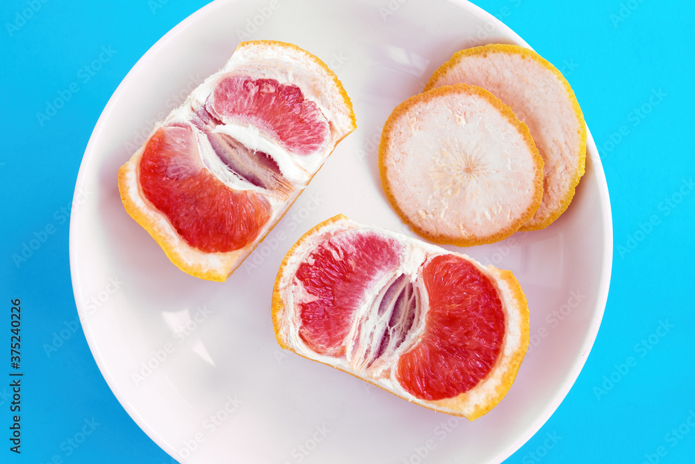 Two halves of sliced grapefruit on white plate on blue background. Diet concept, top view Two halves of sliced grapefruit on white plate on blue background. Diet concept, top view