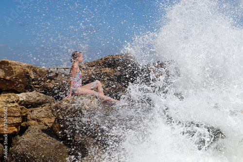 teenage girl sitting on a stone on the seashore under the splashing waves