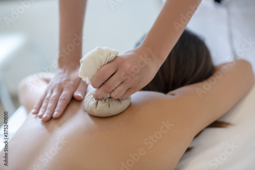 Dark-haired woman having bags ayurvedic massage in salon