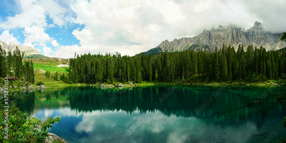 Obraz Panoramic view of Lago di Carezza, pine forest and Catinaccio Mountains reflected on the clear water on a cloudy summer day, Sudtirol, Trentino Alto Adige, Dolomites, Unesco, Italy