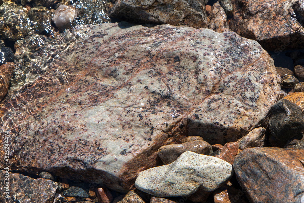 Rocks and pebbles on the shore in the water, various colors and textures Rocks and pebbles on the shore in the water, various colors and textures