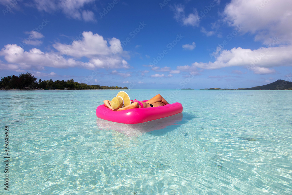 Woman relaxes on pink inflatable on clear turquoise water under the sun during tropical island vacation in Bora Bora Woman relaxes on pink inflatable on clear turquoise water under the sun during tropical island vacation in Bora Bora