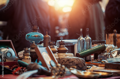 Vintage oil lamps, medals, bottles, trinkets and other goods on the countertop at the sunday flea market. People shopping at the antique bazaar.