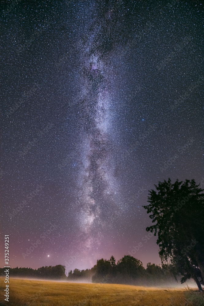 Glowing milky way over crop field covered in fog. Starry night at farmstead. Farm house and tractor. Glowing milky way over crop field covered in fog. Starry night at farmstead. Farm house and tractor.