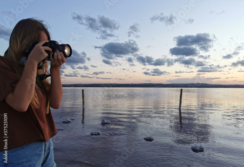 Young Girl takes pictures of the sunset on the lake