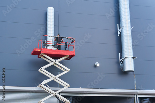 worker assembles the ventilation system of a building using a scissor lift photo