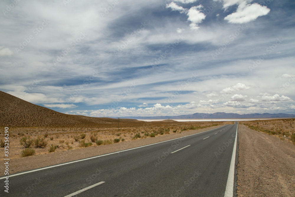 Traveling along the empty desert road. Asphalt highway across the arid valley and mountains under a beautiful sky. 