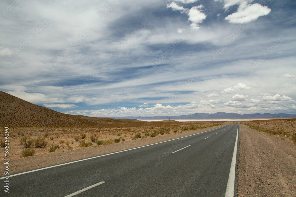Traveling along the empty desert road. Asphalt highway across the arid valley and mountains under a beautiful sky. Traveling along the empty desert road. Asphalt highway across the arid valley and mountains under a beautiful sky.