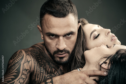 Sexual game and foreplay of three sexual partners. Two beautiful girls foreplay with handsome tattooed bearded man. T group of young sexy attractive two girls and boy. photo