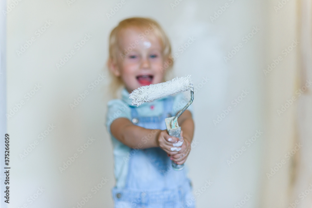 Funny toddler girl holds a white paint roller and smiling in a new house. Selective focus. Funny toddler girl holds a white paint roller and smiling in a new house. Selective focus.