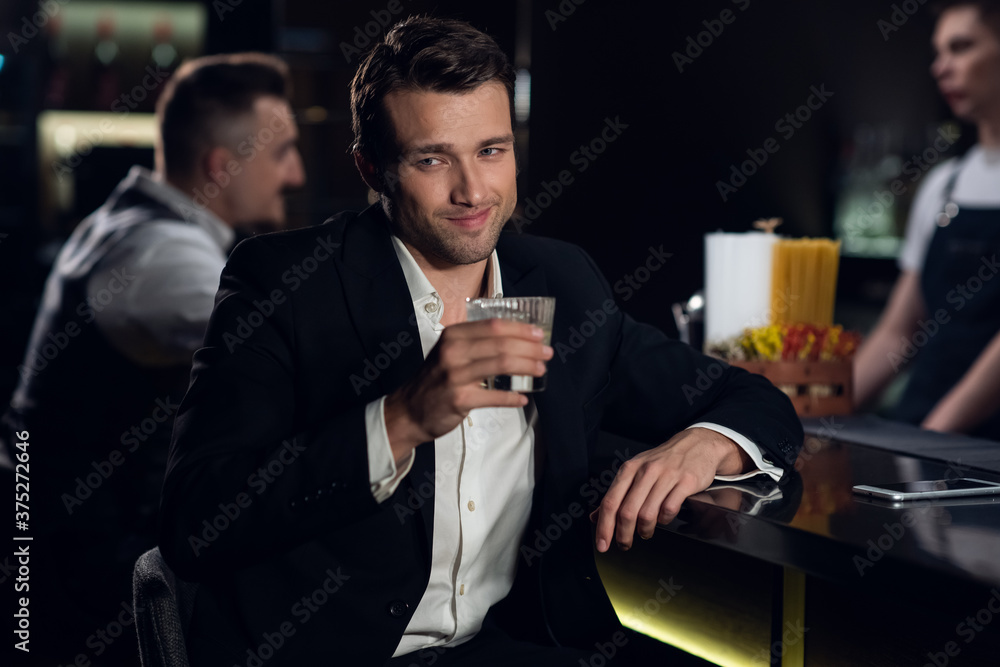 portrait of a young man in a shirt and jacket at the bar with a cocktail in his hands.